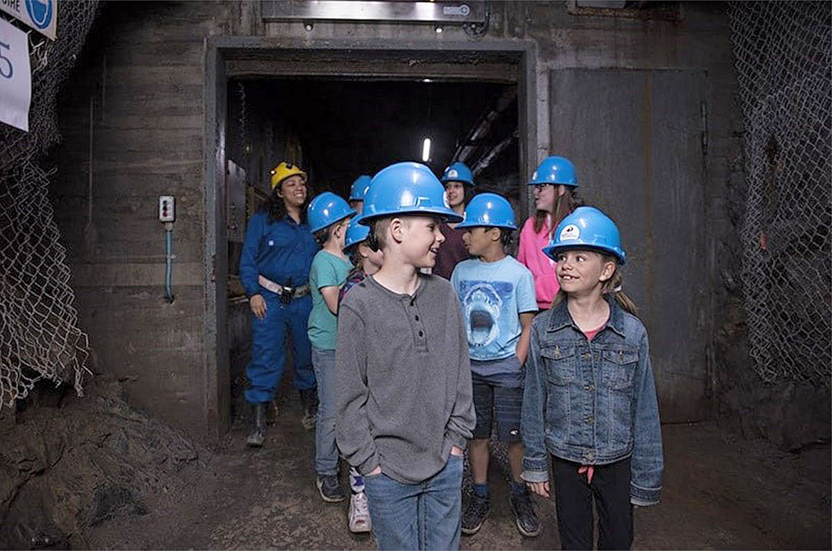Image of an underground mine shaft at Dynamic Earth with children wearing mine helmets walking out of a tunnel.